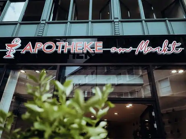 Eingang der Apotheke am Markt in Halle mit modernem Apothekenschild und Pflanzen im Vordergrund