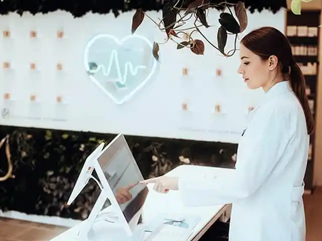 Apothekerin bedient digitales Kassensystem in moderner Apotheke mit Herzsymbol im Hintergrund