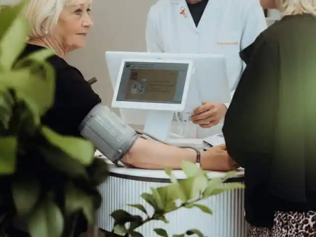 Blutdruckmessung in der Apotheke, ältere Kundin mit Manschette am Arm