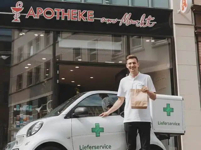 Mitarbeiter der Apotheke am Markt mit Lieferfahrzeug und Medikamententüte vor der Apotheke