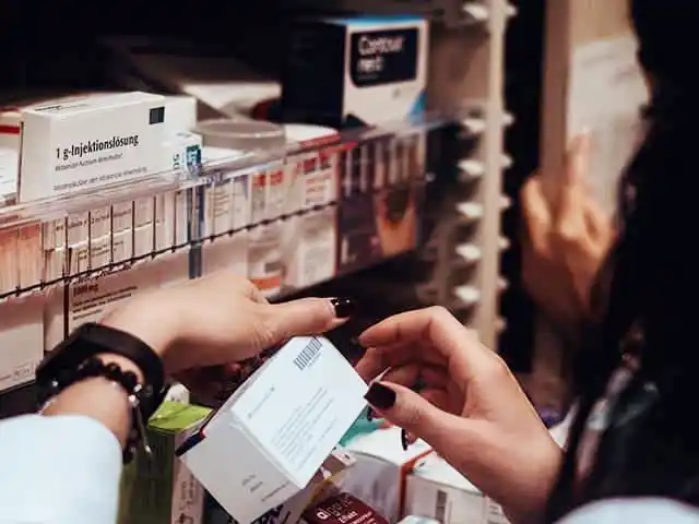 Hände einer Apothekerin, die in der Apotheke eine Medikamentenschachtel aus dem Regal nimmt