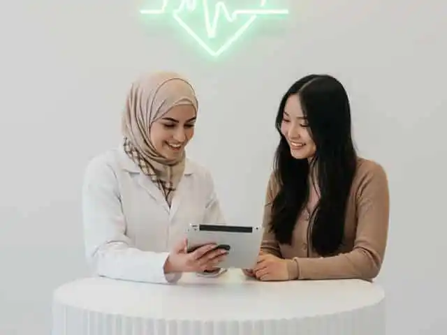 Beratungsgespräch in der Apotheke mit Fachkraft und Kundin, beide schauen gemeinsam auf ein Tablet