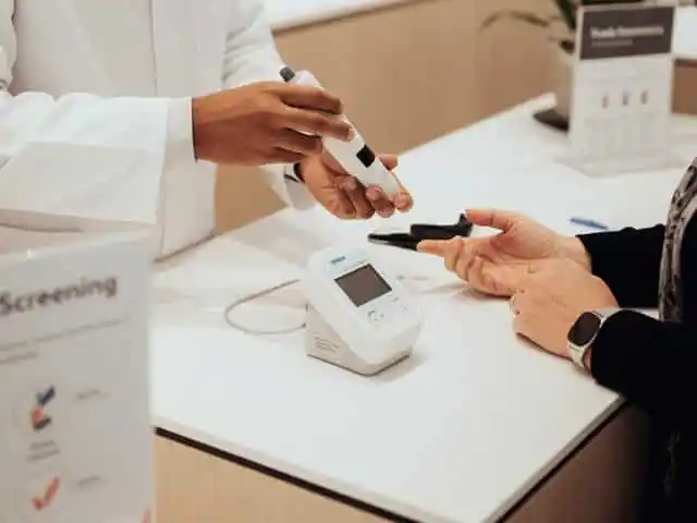 Blutzuckermessung in der Apotheke, Fachpersonal führt Test am Finger durch