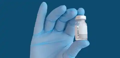 Hand mit blauen medizinischen Handschuhen hält ein Medikamentenfläschchen